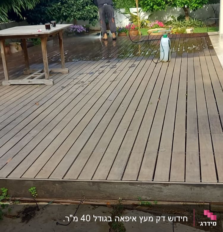 דק עץ עם שולחן, כיסאות ואדם מנקה עם צינור מים